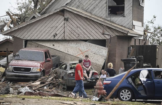 A boy sits on the trunk of a car outside a house which has been wrecked in the storm. Credit: Reuters